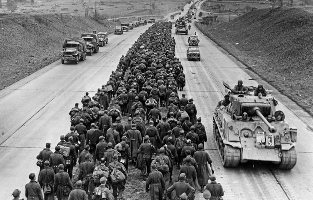 1945_marcius_29_german_pow_s_marching_down_the_autobahn_northwest_of_frankfurt_while_american_troops_advance_to_the_battlefront.png