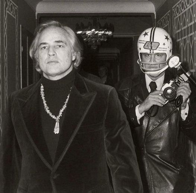 1973_paparazzi_photographer_ron_galella_shown_wearing_a_football_helmet_around_actor_marlon_brando_as_brando_once_sucker-punched_him_broke_his_jaw_and_knocked_out_five_teeth.png