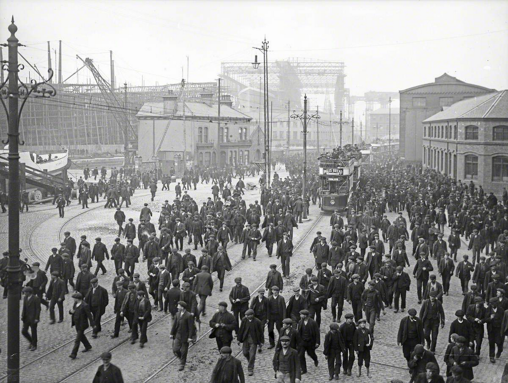 1911_thousands_of_workers_leave_a_shipyard_after_work_in_the_background_the_titanic_can_be_seen_under_construction.png