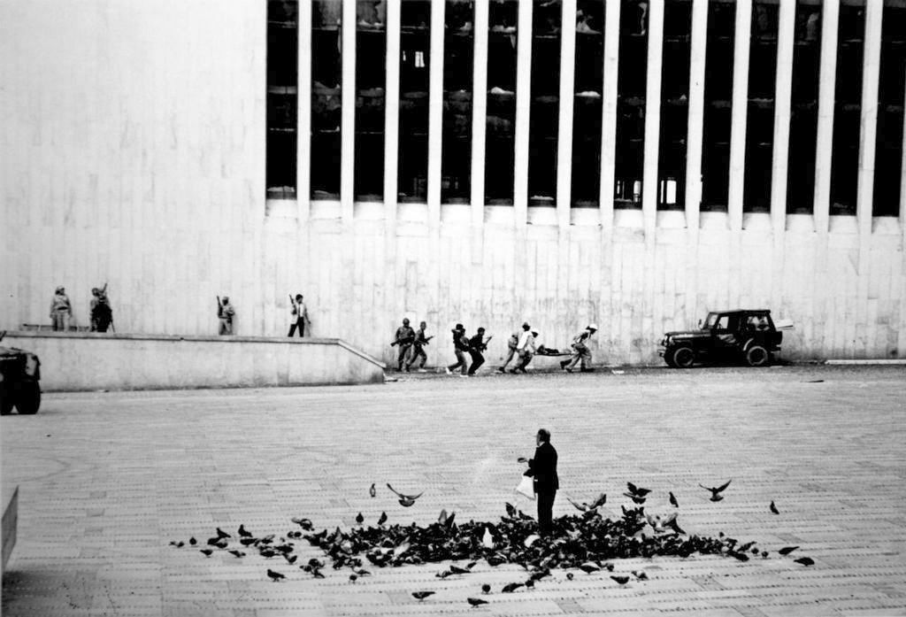 1985_a_man_feeds_the_pigeons_while_the_palace_of_justice_siege_takes_place_in_front_of_him_bogota.jpg