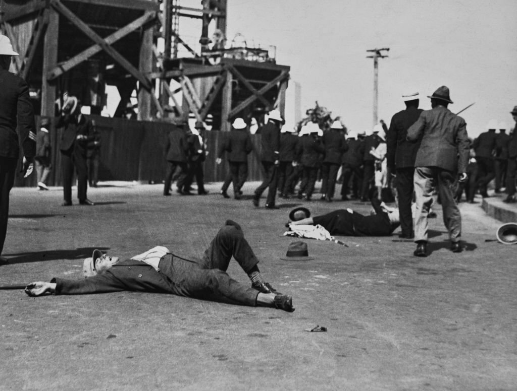 1930_striking_workers_lying_on_the_ground_after_police_wearing_white_helmets_visible_in_the_background_had_dispersed_communist_rioters_who_had_gathered_in_front_of_the_parliament_house_in_sydney.jpg