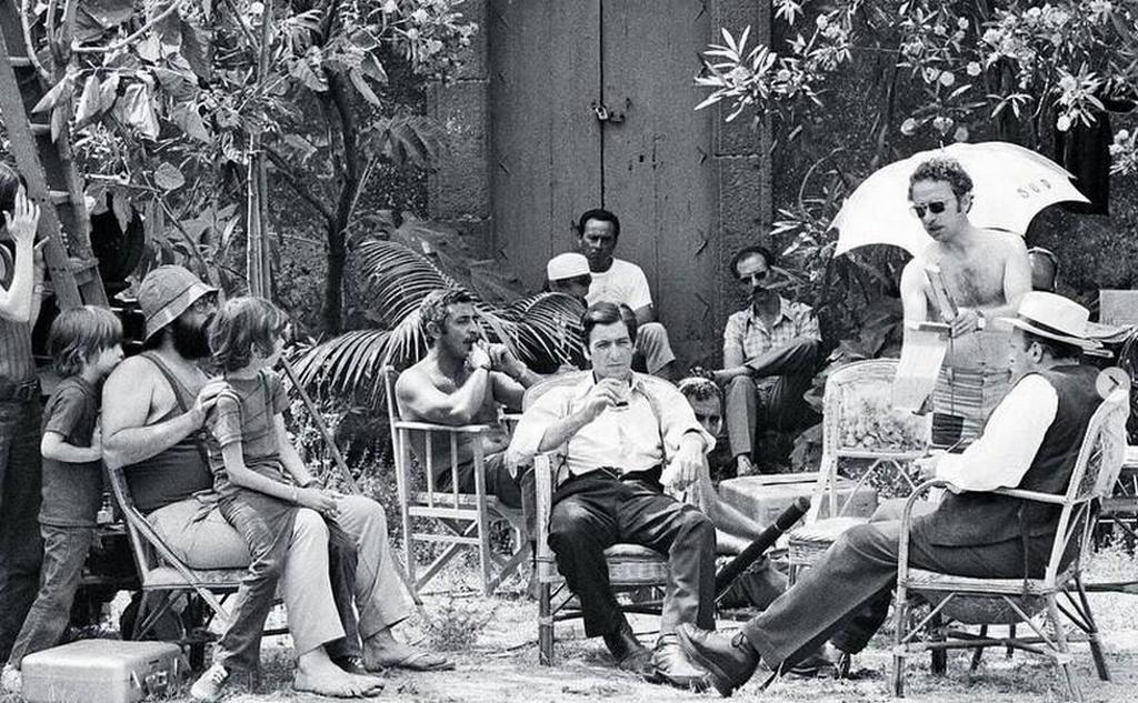 1971_francis_ford_coppola_sitting_far_left_in_hat_and_al_pacino_holding_drink_center_and_some_of_the_cast_of_the_godfather.jpeg