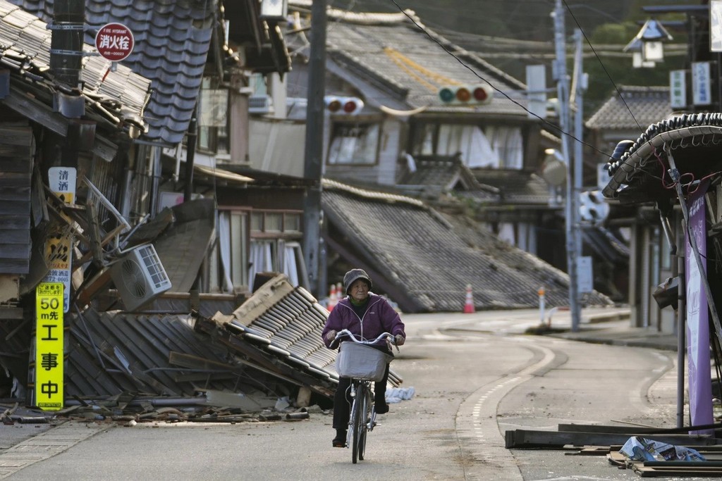 2024_01_02_a_woman_bikes_amid_damaged_houses_in_noto_town_in_the_noto_peninsula_facing_the_sea_of_japan_northwest_of_tokyo_ap_photo_hiro_komae.jpg