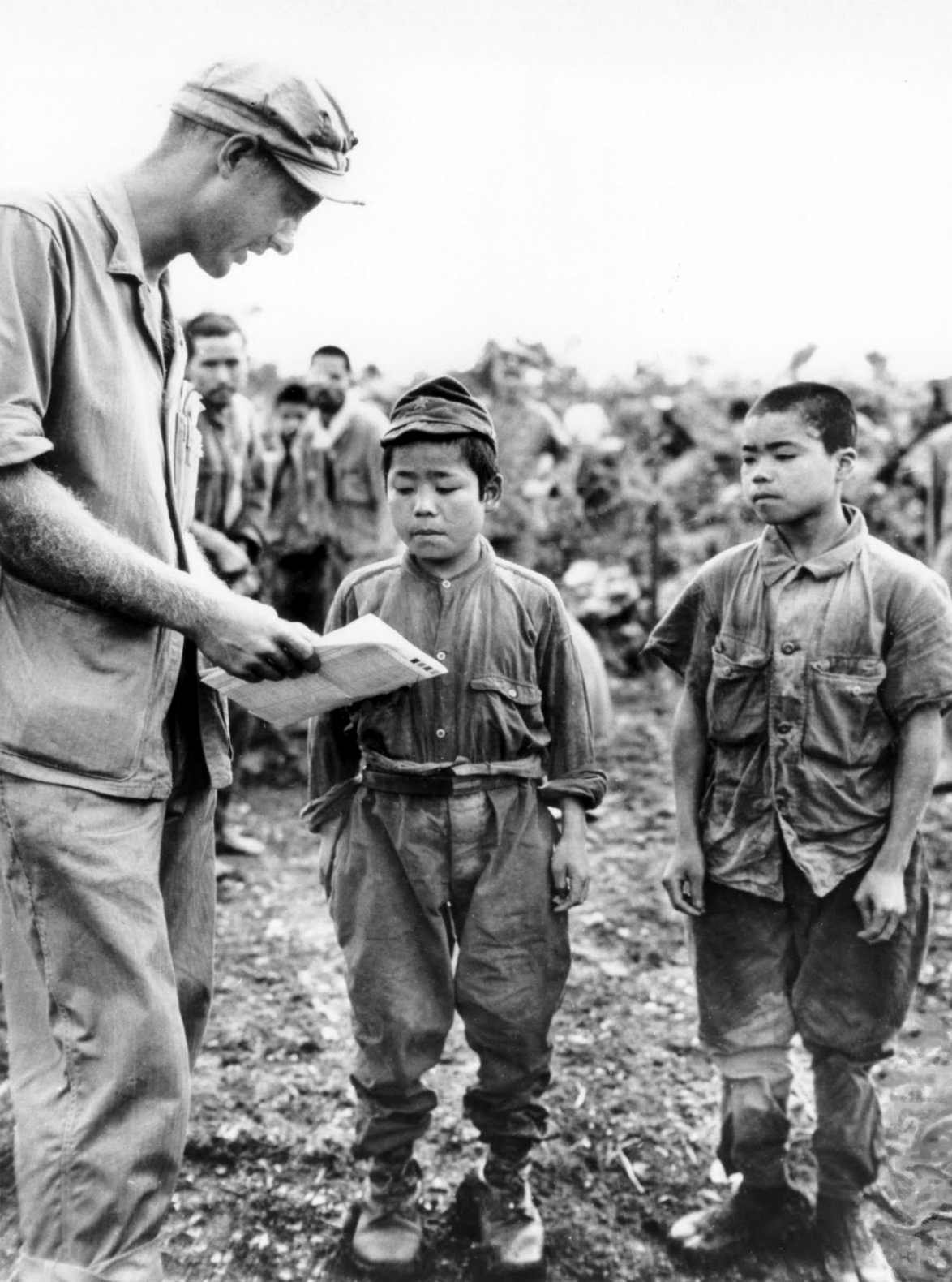 1945. június. U.S. Marine 1st Lt. Hart H. Spiegal própál kommunikálni két japán gyerekkatonával Okinawán..jpg