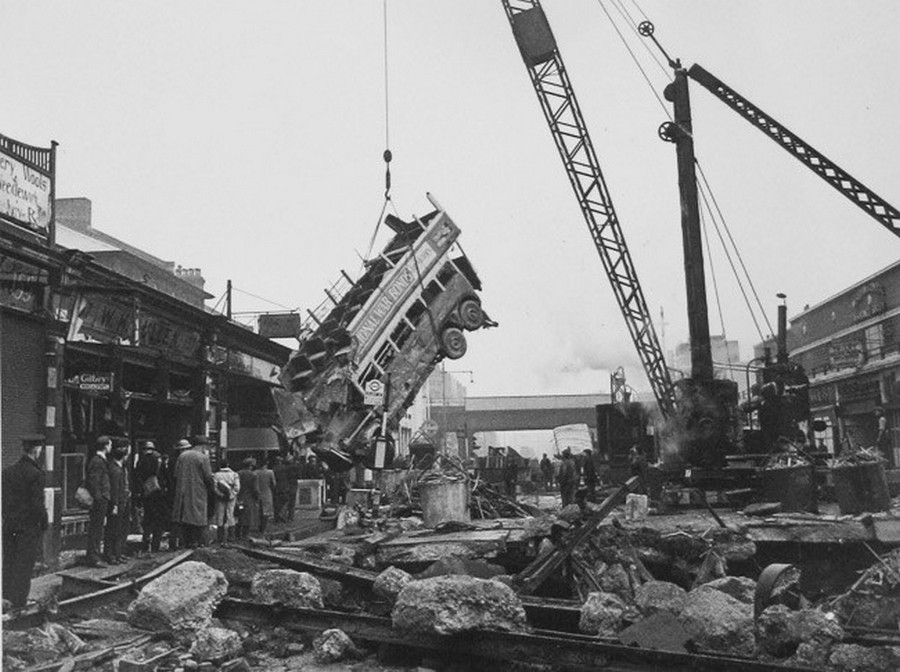 1940. október. A Balham High street éjszakai bombázásától beszakadt az utca alatti aluljáró menyezete és a 88-as busz az elsötítés miatt a bumbakráterbe esett. A képen a roncs másnapi kiemelése látható..jpg