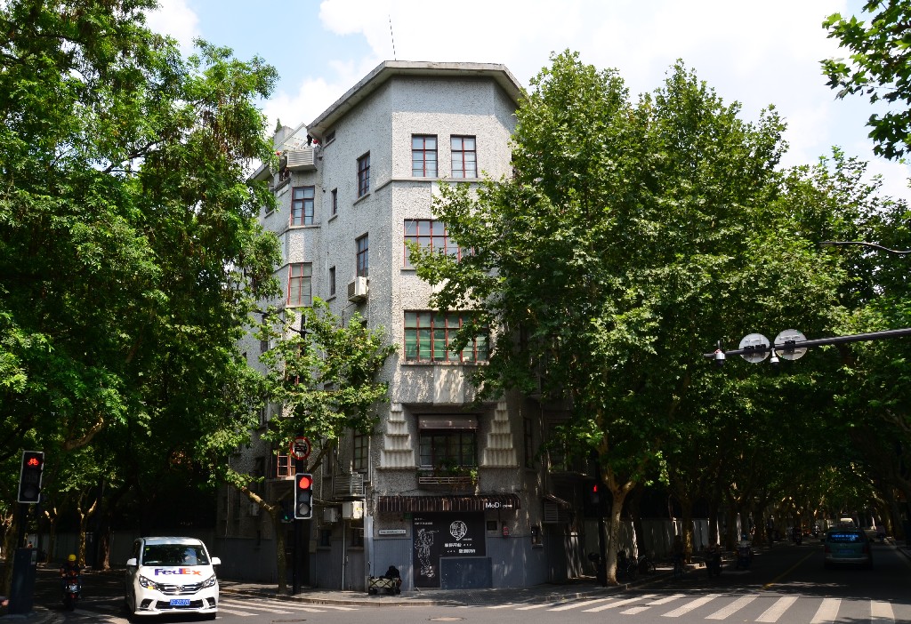 115. szám: Midget Apartment<br />A Midget Apartments egy lenyűgöző Art Deco épület a Wukang és Hunan utcák találkozásánál. 1931-ben építették és akkor az újságok Sanghaj legegyedibb, sőt legfurcsább apartmanházának nevezték.<br />Marcel Guillet, a Credit Foncier d‘Extreme Orient nevű cég főépítésze tervezte. A vasaló alakú lakóépület ötemeletes, minden emelet egy teljes lakásból áll: előszoba, két szoba, konyha, fürdőszoba és cselédszoba. Az ötödik emeleten egy műterem lett kialakítva.