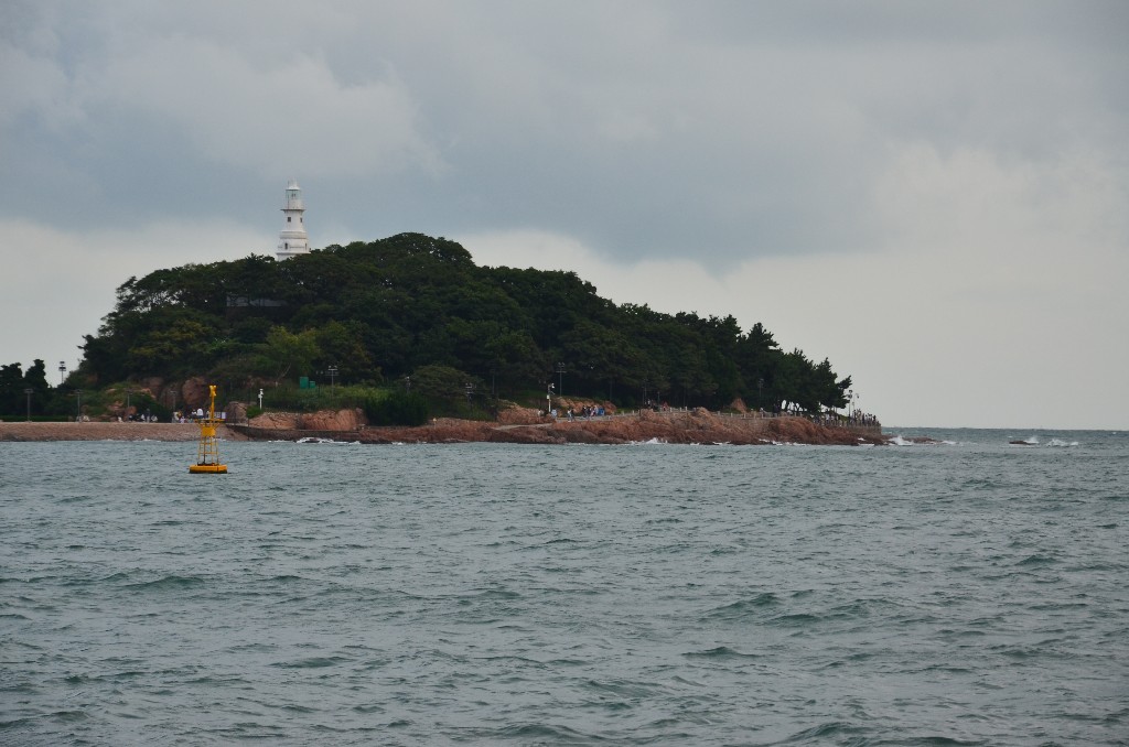 A Qingdao -szigetet tengerfal köti össze a szárazfölddel.<br />1987-ig zárt katonai terület volt. A német megszállás alatt, a ‘Qingdao‘ nevet adták neki és 1890-ben világítótornyot építettek rá, amit csak 1915-ben kezdtek használni. A nyolcszögletű, 16 méter magas, fehér márványból épült világítótorony a Jiaozhou- és a Qingdao-öbölbe érkező és onnan kilépő hajókat kalauzolja.<br />1914 után a japánok megtámadták és elfoglalták a Jiaozhou -öblöt, a Xiao Qingdao -t átkeresztelték ‘Kato -szigetre‘.<br />Mivel a sziget alakja olyan, mint egy kínai citera ‘Qin Dao‘-nak is szokták nevezni.<br />A szigetet sétaútvonalak ölelik át, belsejében szép parkot alakítottak ki, virágos növényekkel, szobrokkal, pavilonokkal, kávézókkal. Megvannak még a japánok által épített torpedó garázsok is.