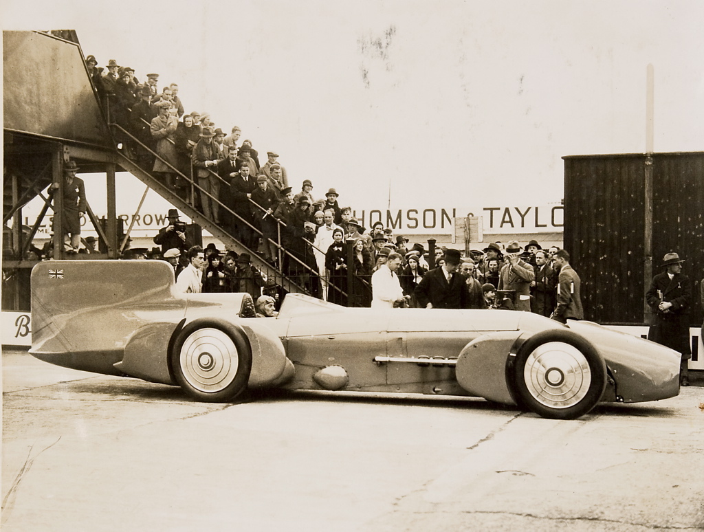 Sir_Malcolm_Campbell_at_the_wheel_of_the_-Bluebird-,_with_crowd,_1926_-_1936.jpg