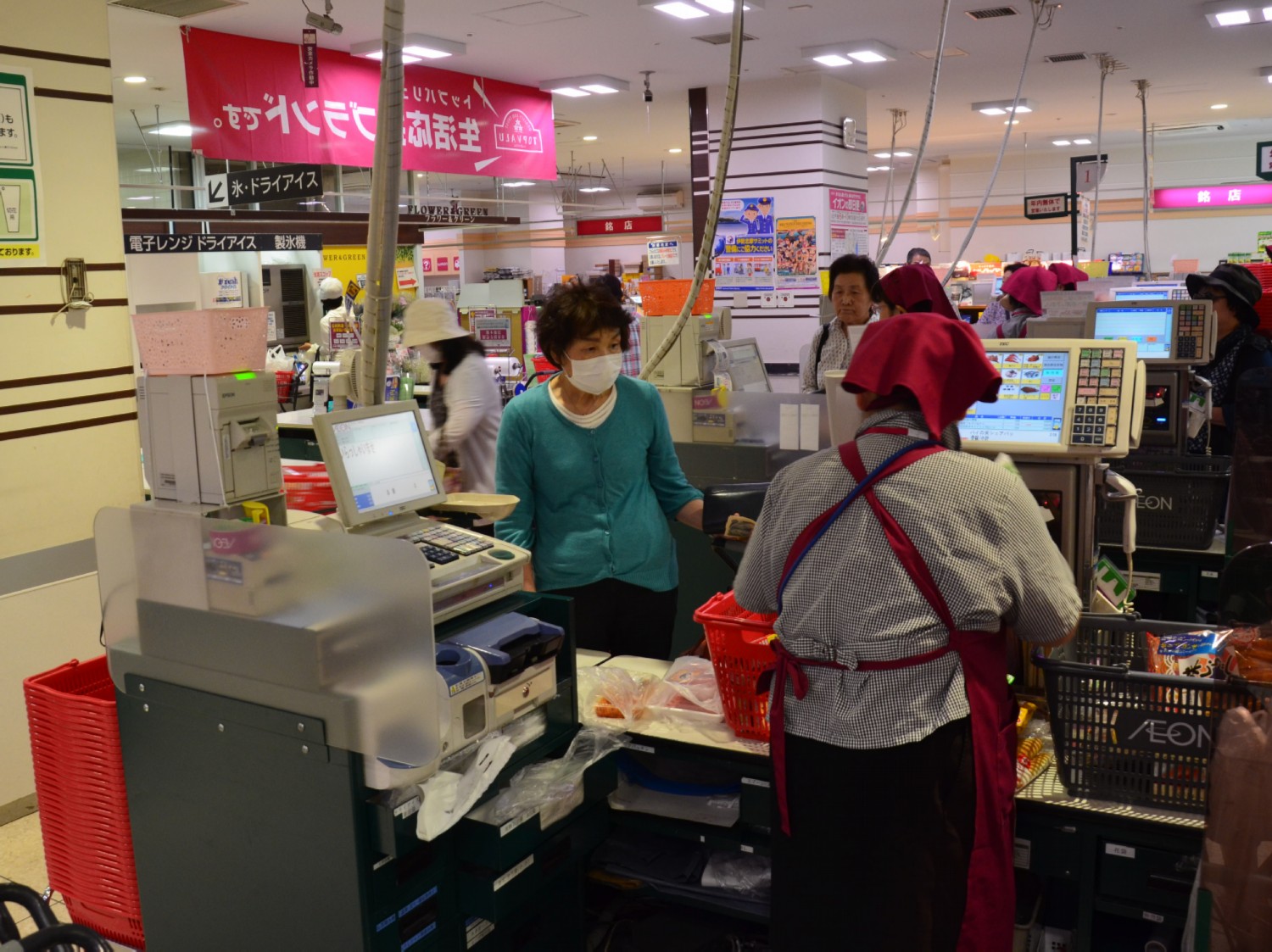 A kovetkezo kepek az AEON penztaraknal keszultek. Ket monitor lathato, egyiken a leolvasott cikkek jelennek meg, majd a vegosszeg, aztan ez megjelenik a kassza gepen es ott tortenik a fizetes. Ha keszpenzzel fizetunk hangosan leszamolja a visszajarot, a papirpenzt a kezunkbe adja, az aprot kulon kis tanyerkaba teszi.